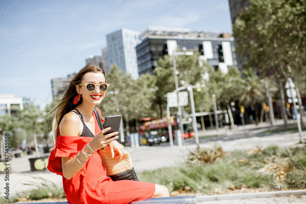 一位穿着红色连衣裙、拿着电话的商务女性坐在户外现代办公室的生活方式画像