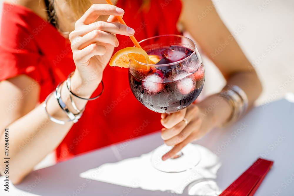 一位女士拿着一杯由葡萄酒制成的西班牙传统酒精饮料Sangria，坐在户外