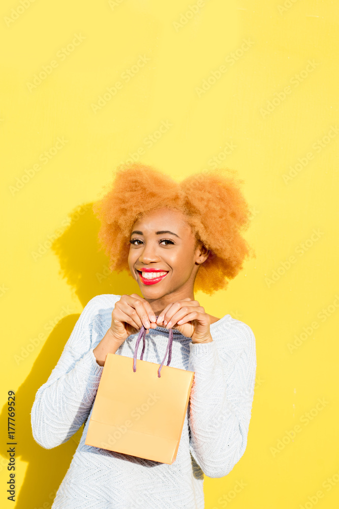 Portrait of a beautiful african woman in blue sweater standing with shopping bag on the yellow backg