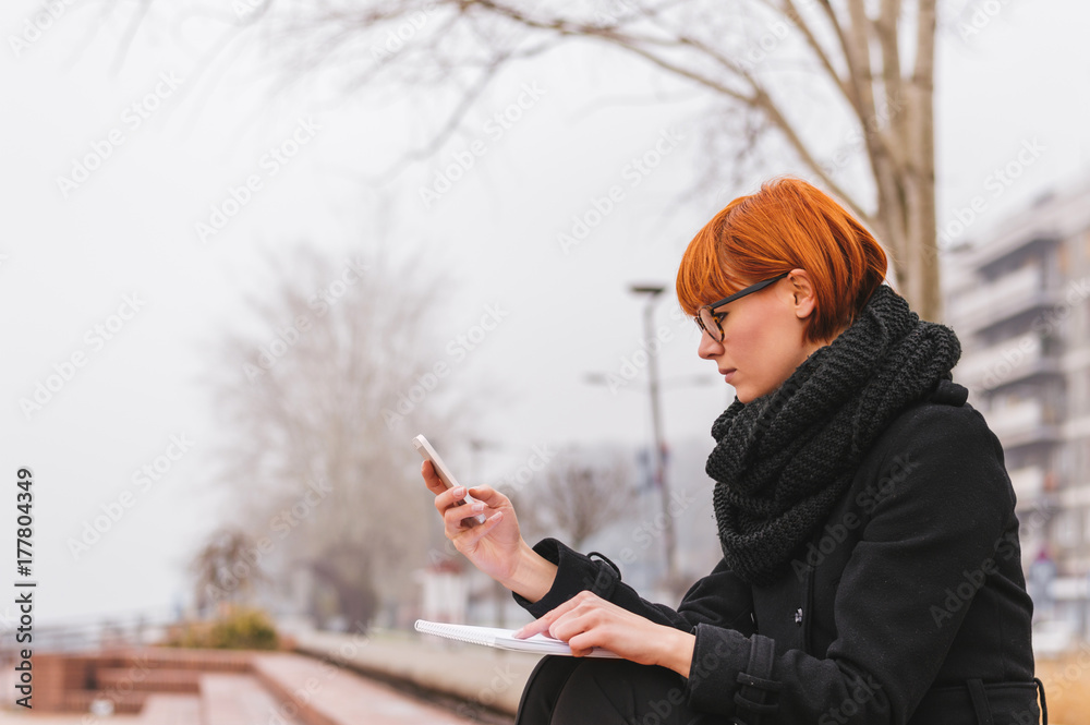 女孩冬天在户外使用手机。通过智能手机发短信。