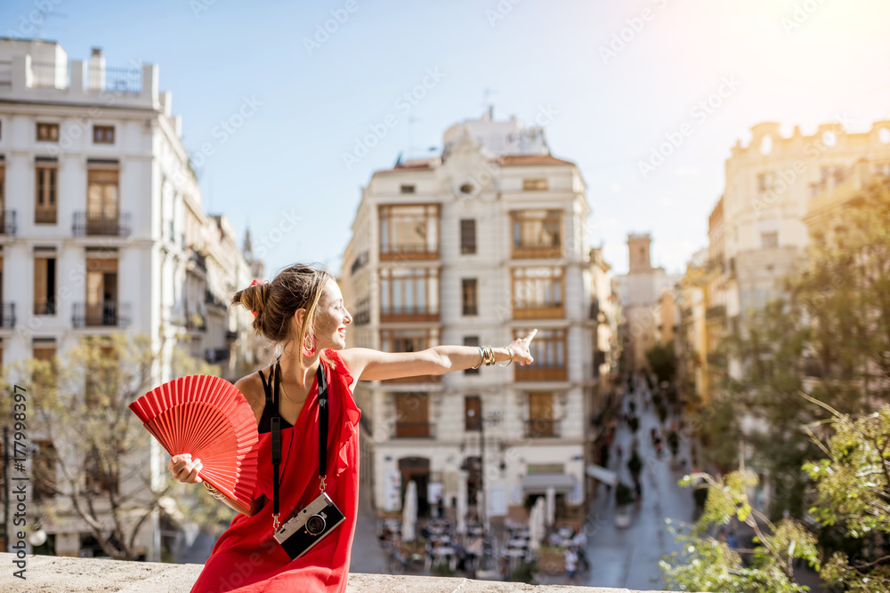 年轻女子身穿红色连衣裙，手持扇子和相机，在Valenci欣赏美丽的城市景观