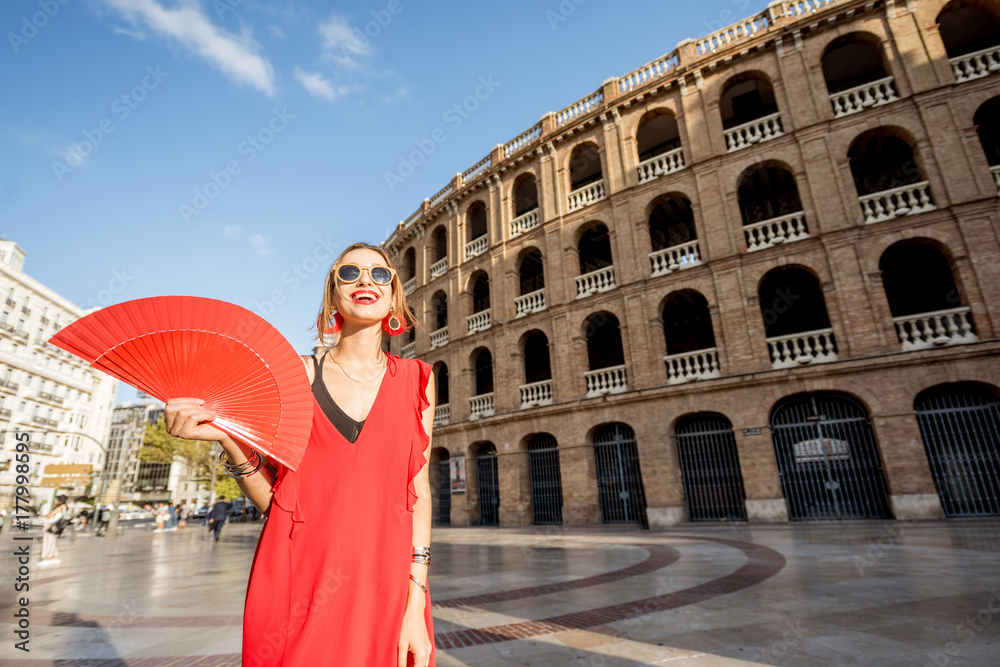 Portrait of a woman in red dress with spanish hand fan stnading in front of the bullring amphitheatr