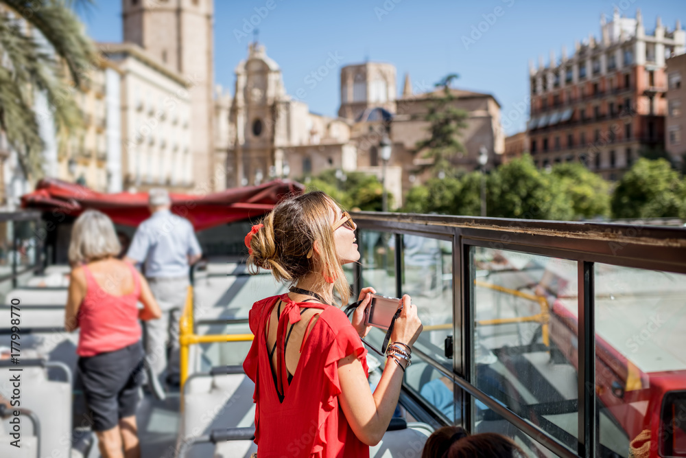 Young happy woman tourist in red dress having excursion in the open touristic bus in Valencia city, 