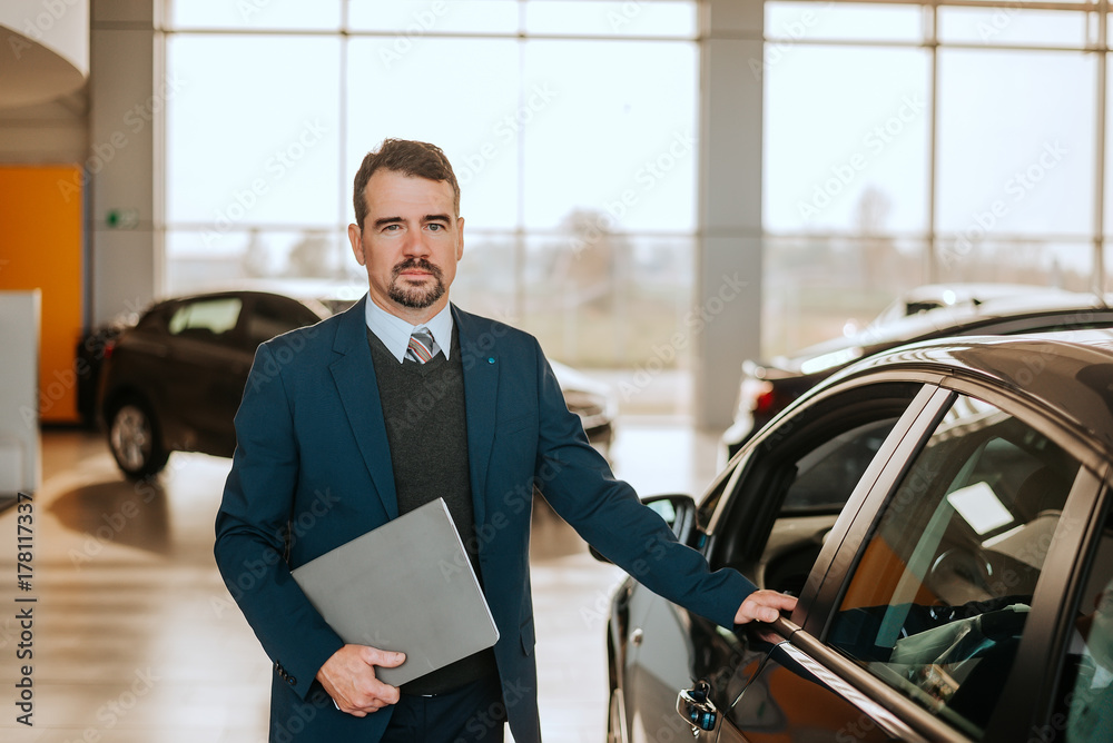 Portrait of senior vehicle salesman working at a car dealer.