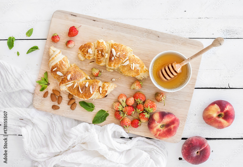 Freshly baked almond croissants with garden strawberries, peaches, mint and honey on serving board o