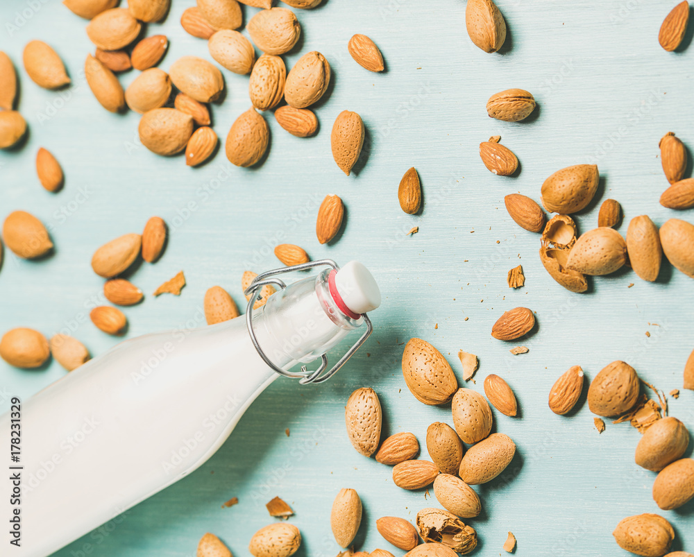 Dairy alternative milk. Almond milk in glass bottle and fresh nuts over blue background, top view, s