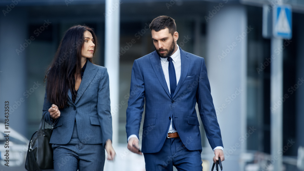 商务女性和商务男性穿着定制西装走在繁忙的大城市街道上。