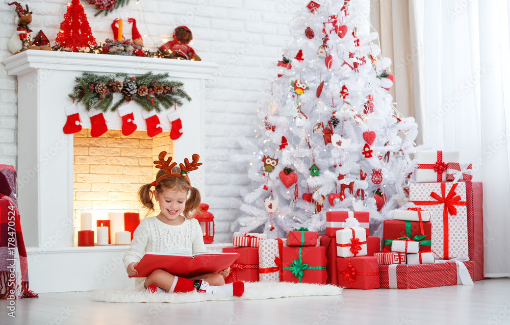 happy child girl reading book in morning at Christmas tree