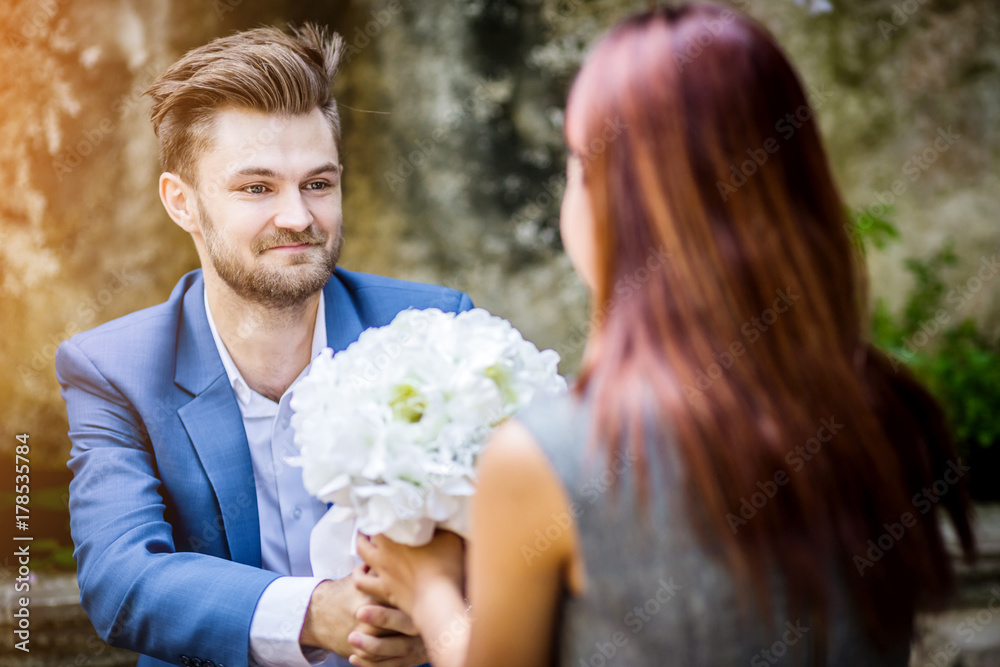 肖像年轻人在花园里用白花向千禧一代女友求婚