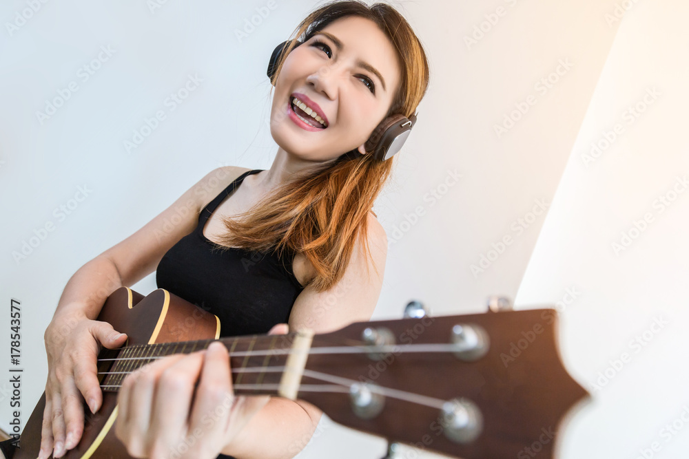 beautiful Asian Woman Playing Ukulele with happiness and joyful near widow white room background