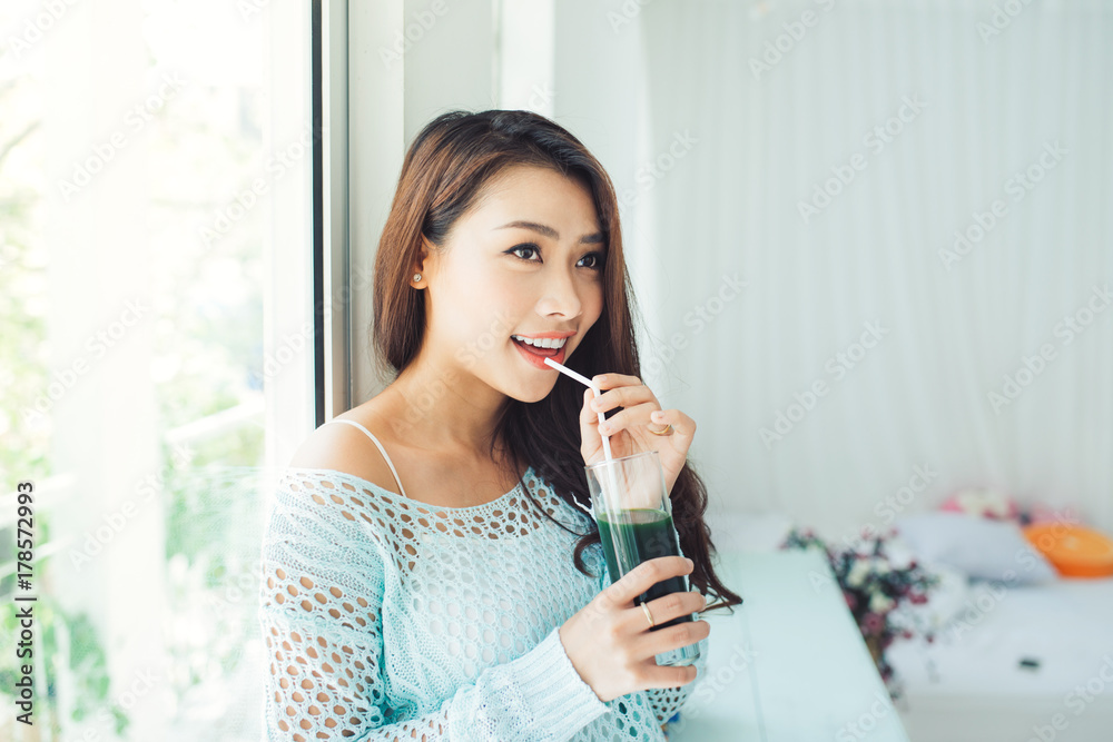 漂亮的年轻亚洲女人在家喝绿色新鲜蔬菜汁或冰沙