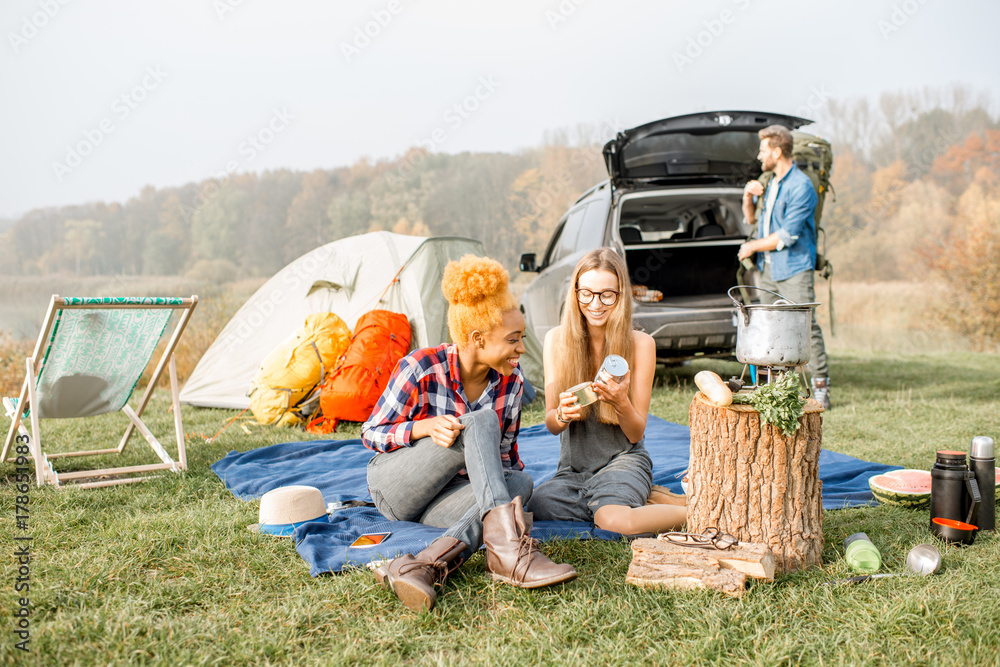 Multi ethnic group of friends dressed casually having a picnic during the outdoor recreation with te