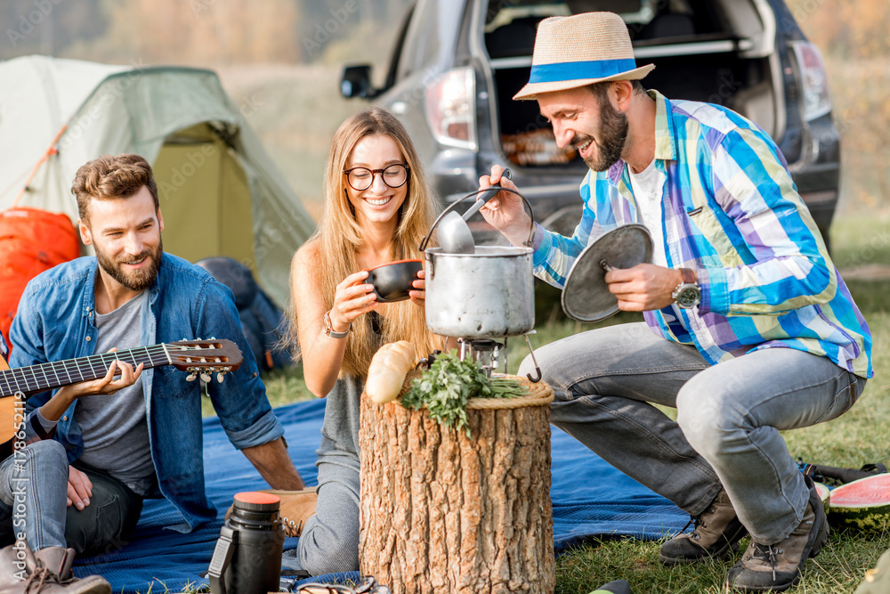 Multi ethnic group of friends dressed casually having a picnic, cooking soup with cauldron during th