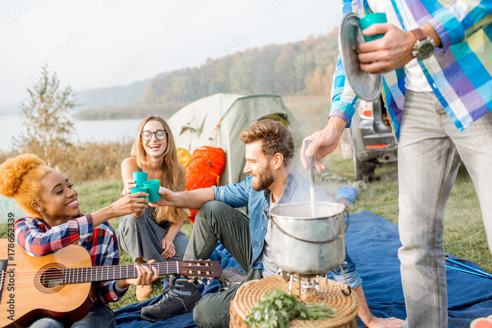 Multi ethnic group of friends dressed casually clinking glasses during the dinner outdoors at the ca