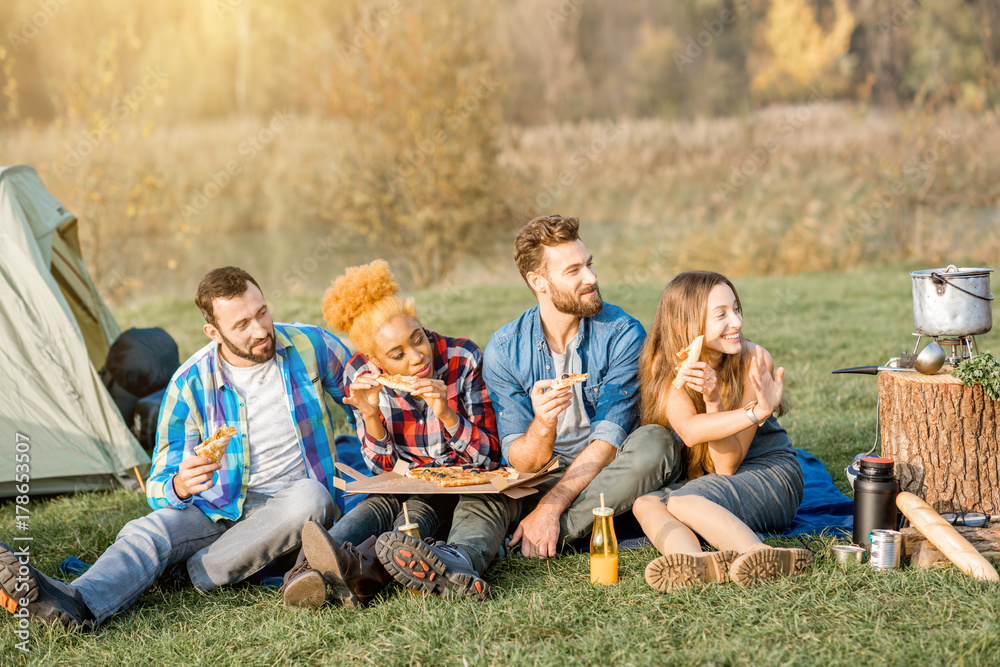 Multi ethnic group of firends dressed casually having fun eating pizza during the outdoor recreation