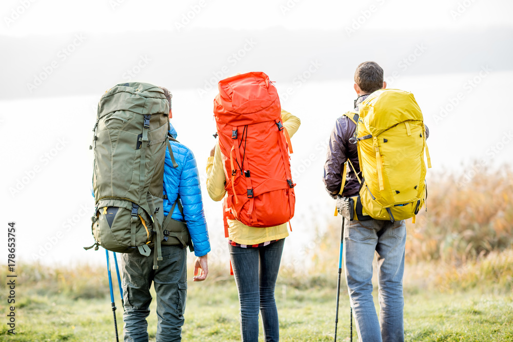 雾天，一群背着五颜六色背包的徒步旅行者站在湖边