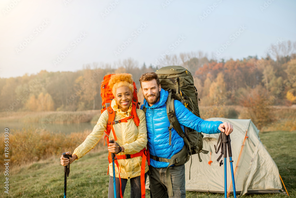 美丽的多民族夫妇背着背包和棍子站在露营地徒步旅行的肖像