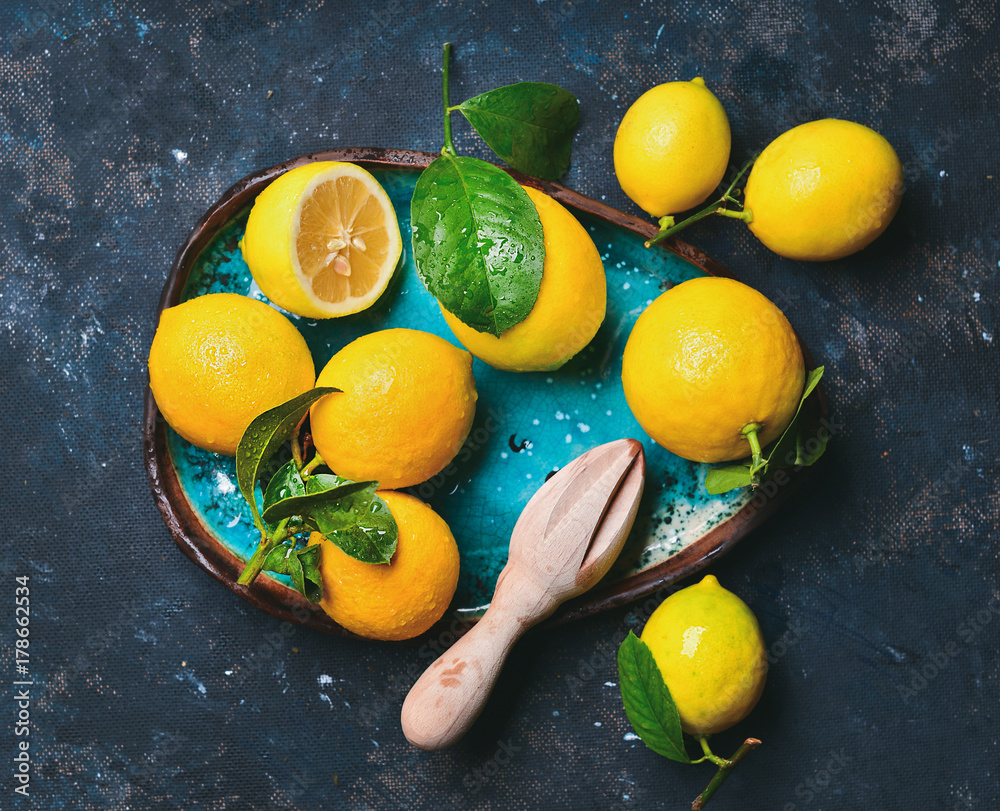 Freshly picked lemons with leaves in blue ceramic plate over dark blue shabby background, top view