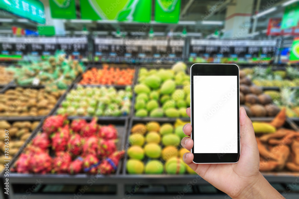 Hand holding smartphone with white blank screen and blurred supermarket fruit background