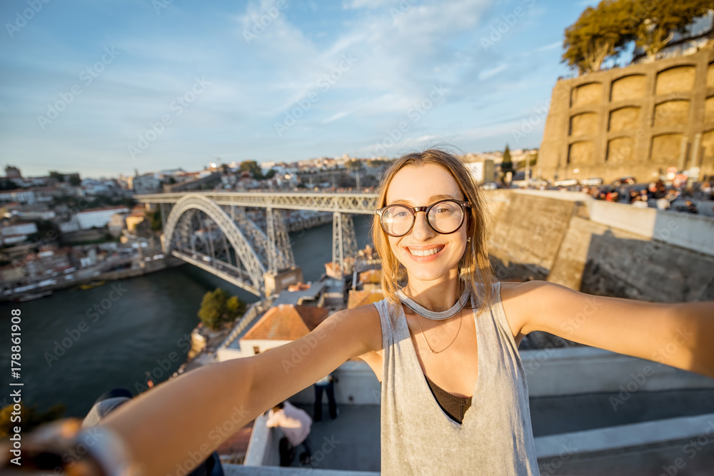 Young woman tourist making selfie photo on the beautiful cityscape background during the sunset in P