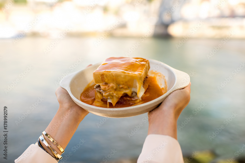 Holding a plate with traditional portuguese sandwich with meat called francesinha on the landscape b