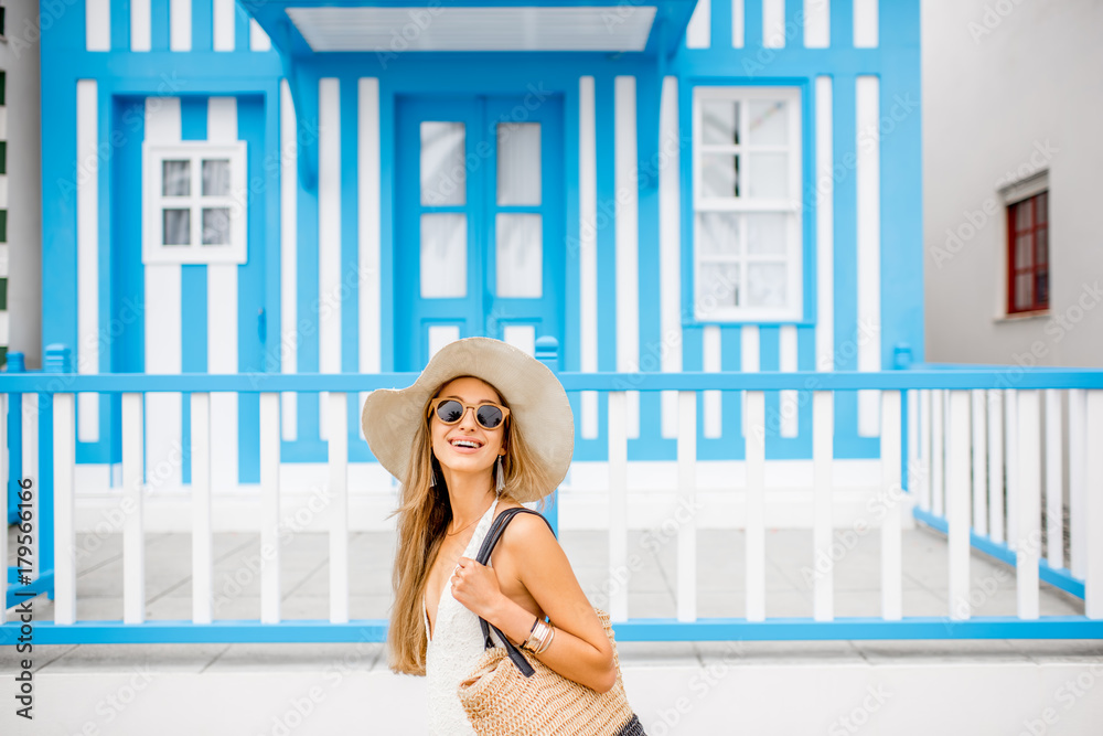 Young woman in swimsuit and sun hat standing with old traditional blue striped house on the backgrou