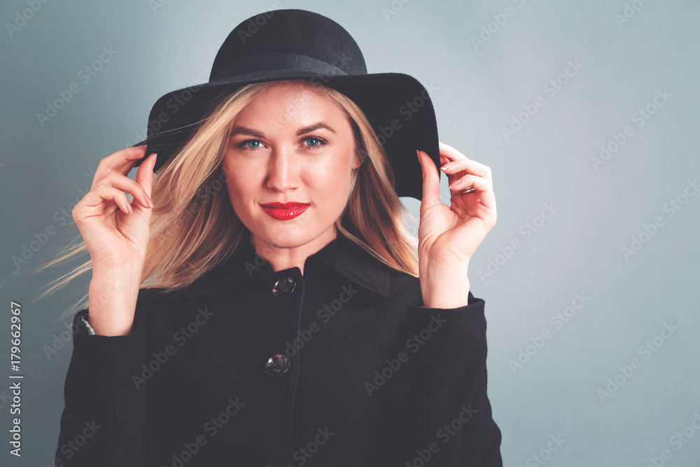 Beautiful young blonde woman in a black coat on a gray background