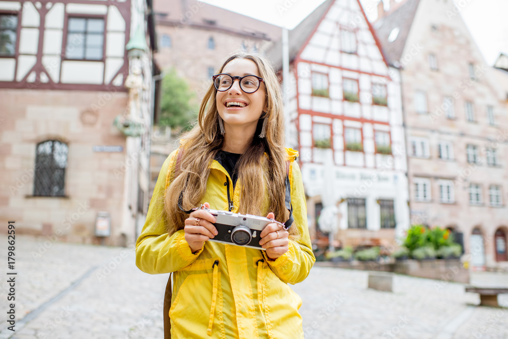 Young woman tourist in yellow raincoat standing with backpack on the old square with beautiful build