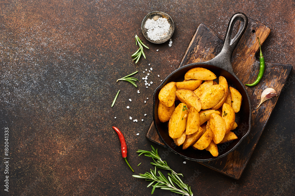 Roast potato with salt and spices in pan on wooden board on brown background with copy space. Top vi