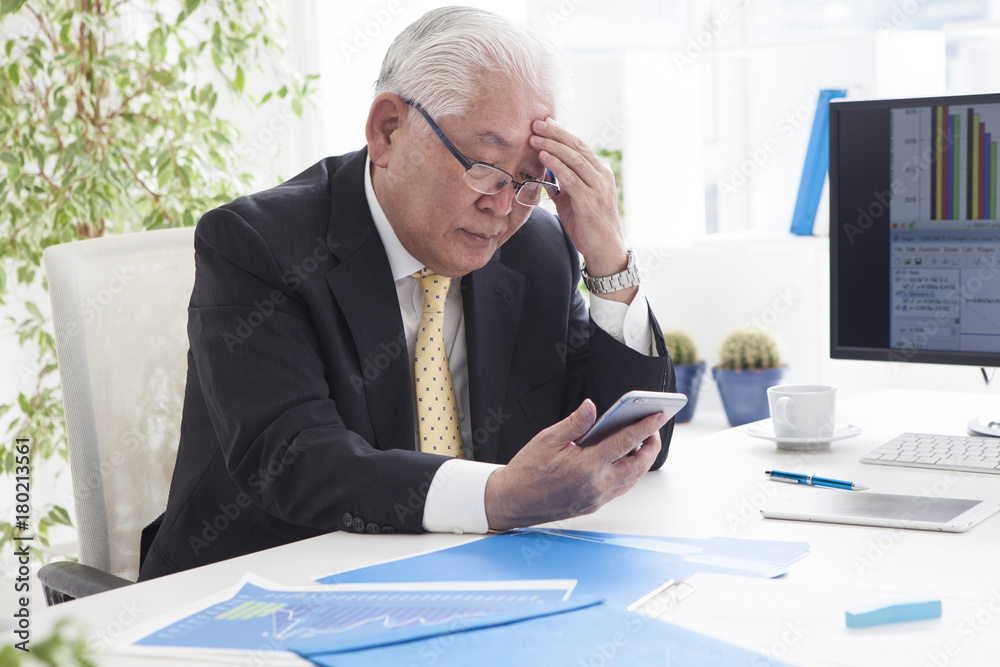 An old man looking at a smartphone and having a troubled face