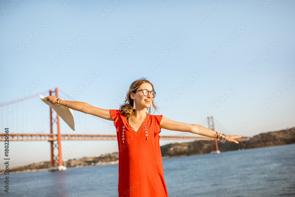 一个女人站在河边玩得很开心，在Lisbo的铁桥上可以看到美丽的景色