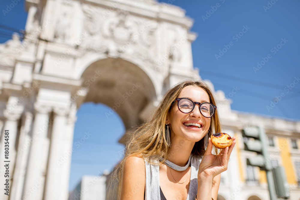 户外凯旋门上，一位年轻女子拿着一种名为pastel de Nata的葡萄牙蛋挞糕点