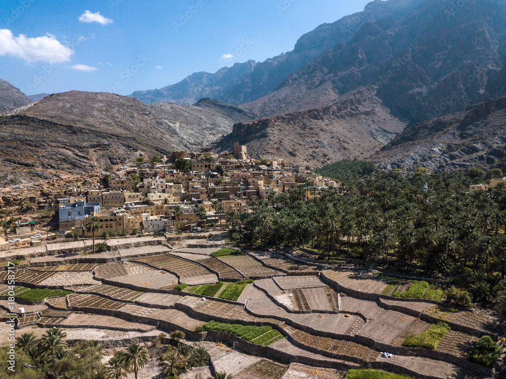 Aerial drone view of an old traditional Omani mud village in the mountains among date palm trees. Ba