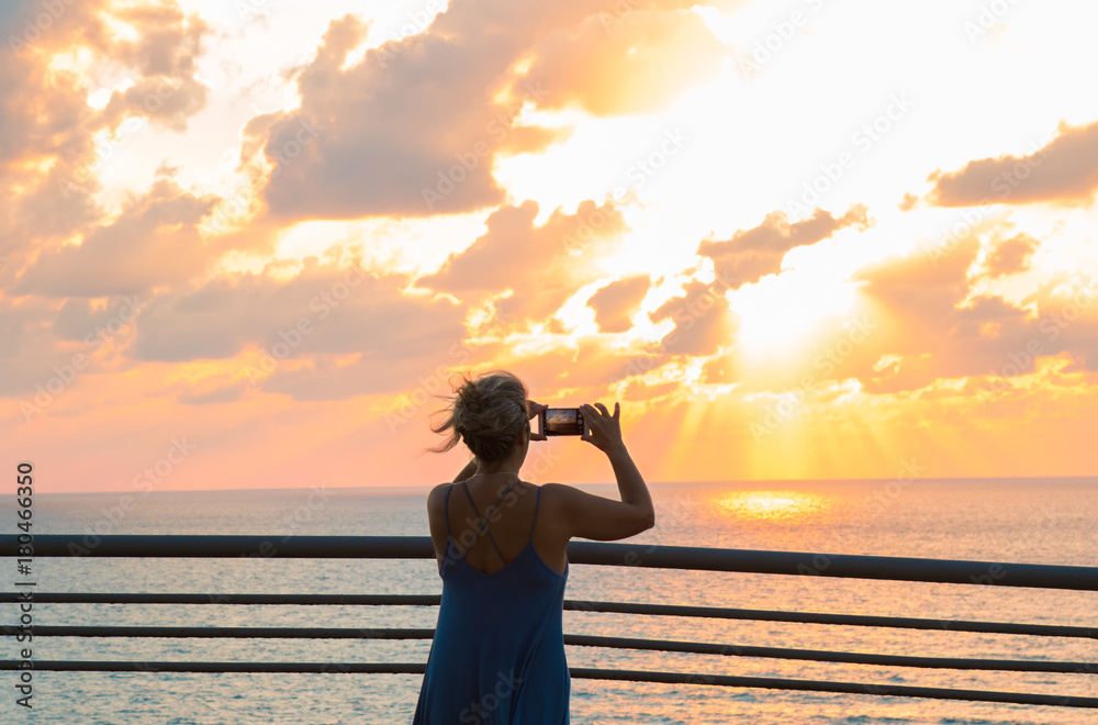 Female  photograph sunset on the phone at the sea.