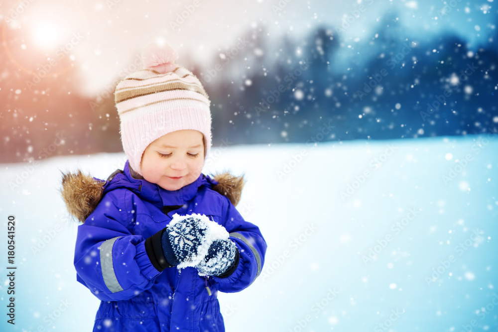 女婴在雪中行走。穿着冬装的孩子在玩雪