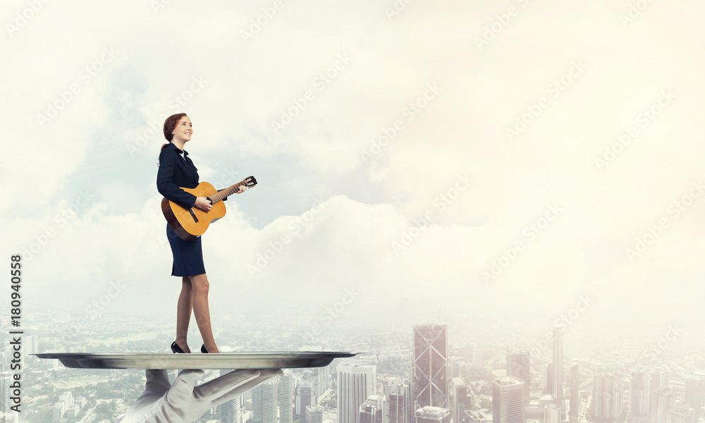 Attractive businesswoman on metal tray playing acoustic guitar against cityscape background