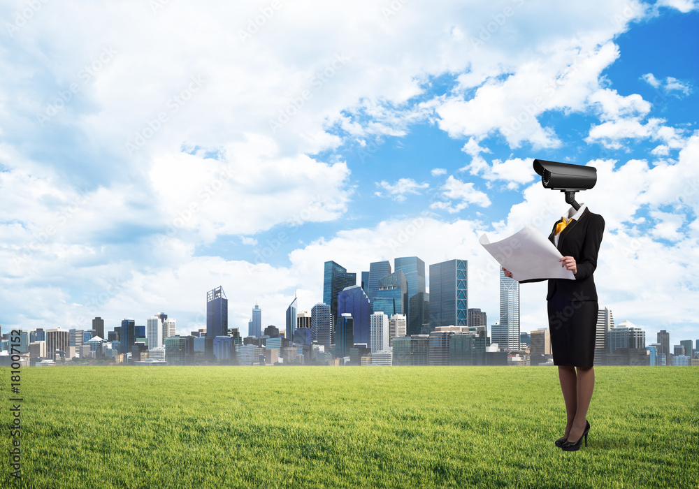 Camera headed woman standing on green grass against modern cityscape