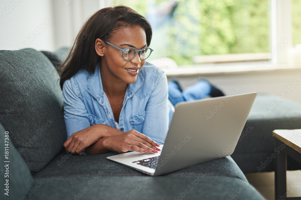 Young African woman lying on her sofa using a laptop