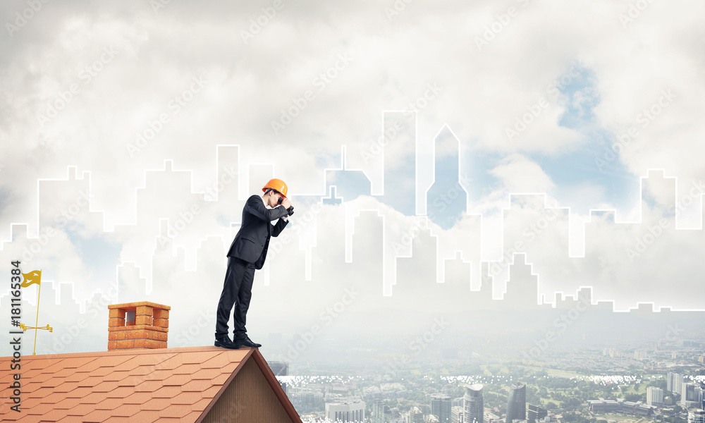 Engineer man standing on roof and looking in binoculars. Mixed m