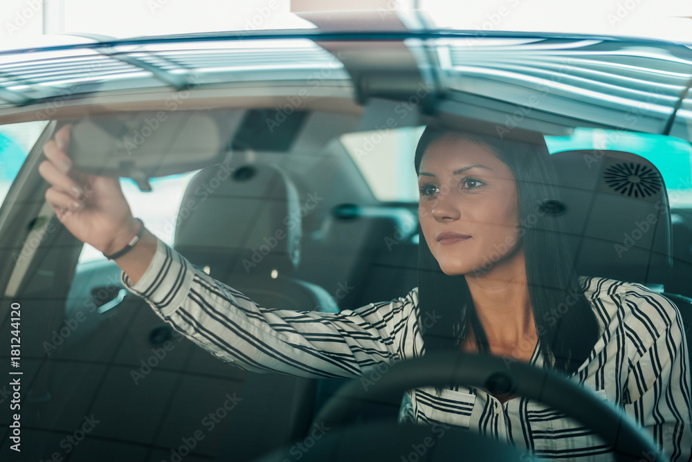 Beautiful woman sitting in car, adjusting car mirror.