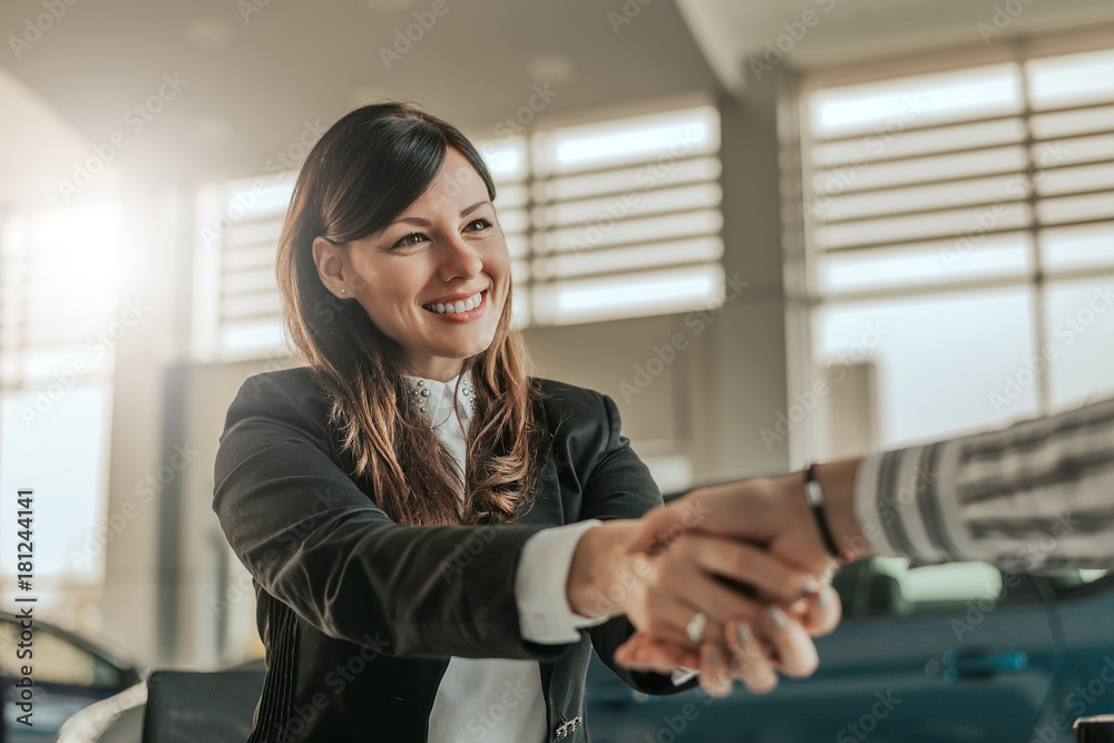 Cheerful car dealer handshake with customer in showroom.