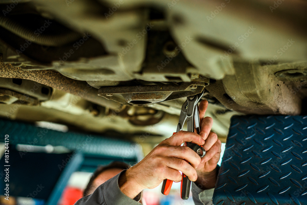 Car mechanic under a car in repair service.