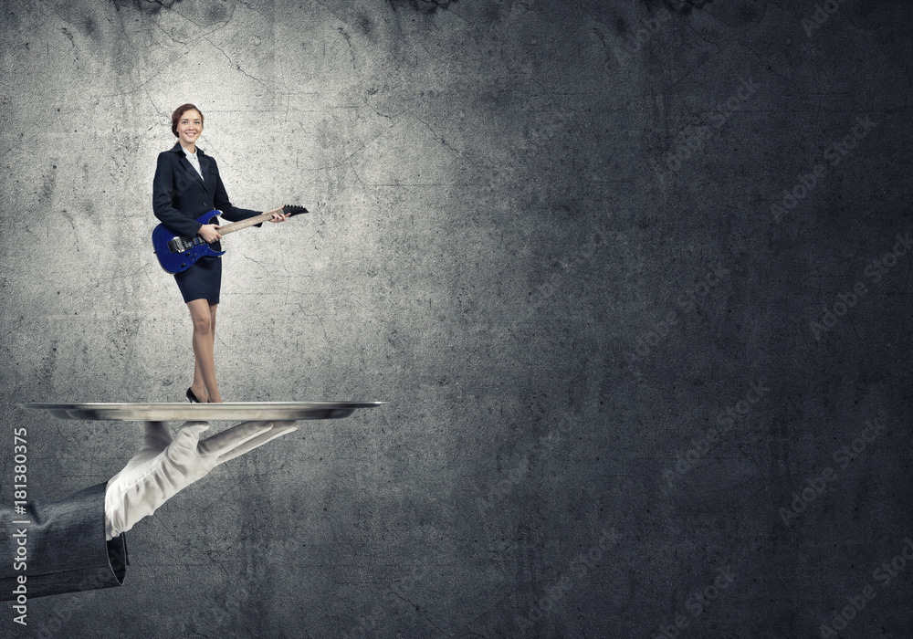 Attractive businesswoman on metal tray playing electric guitar against concrete wall background