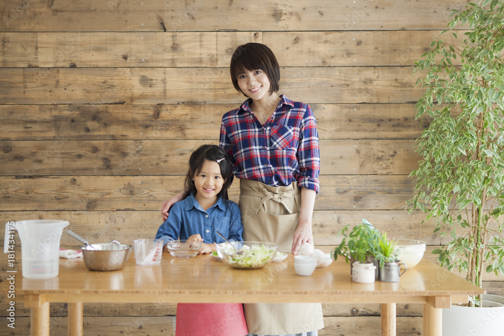 可爱的小女孩和她美丽的妈妈。他们在家的厨房里做饭时面带微笑。