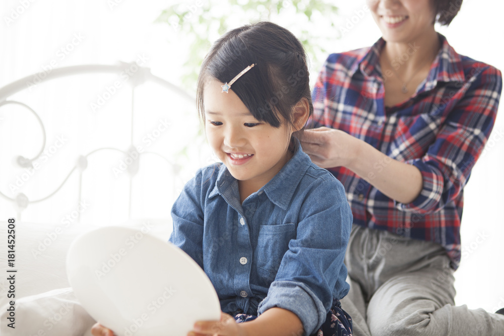 In the bedroom, a young mother is tying her daughters hair.