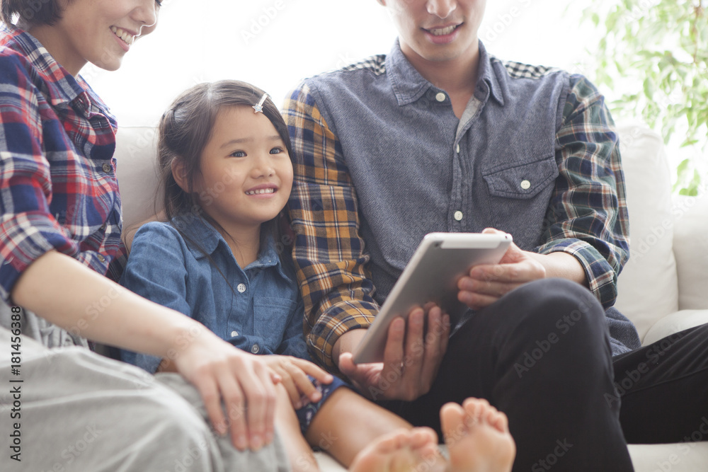 Parents and daughter are sitting on the sofa and using a digital tablet together.