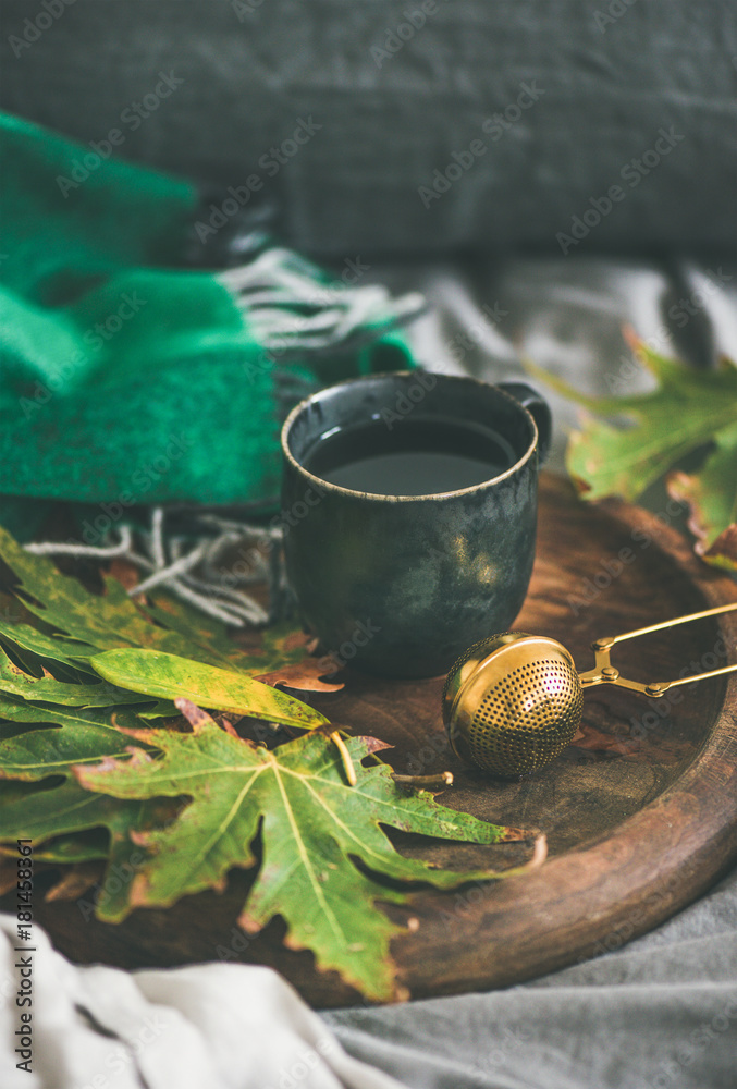 秋天的早茶躺在床上。一杯带筛子的红茶和乡村木地板上五颜六色的落叶