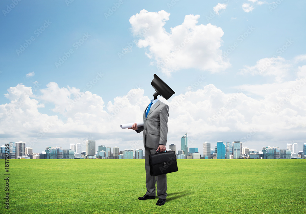 Camera headed man standing on green grass against modern cityscape