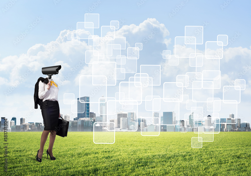 Camera headed woman standing on green grass against modern cityscape