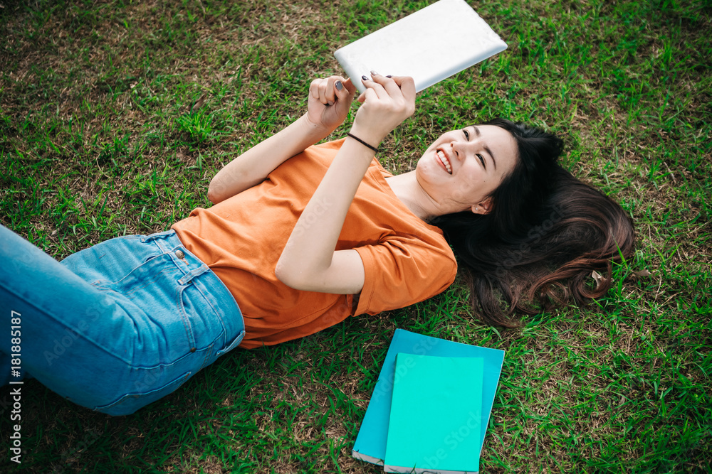 A young or teen asian girl student in university smiling and reading the book and look at the tablet